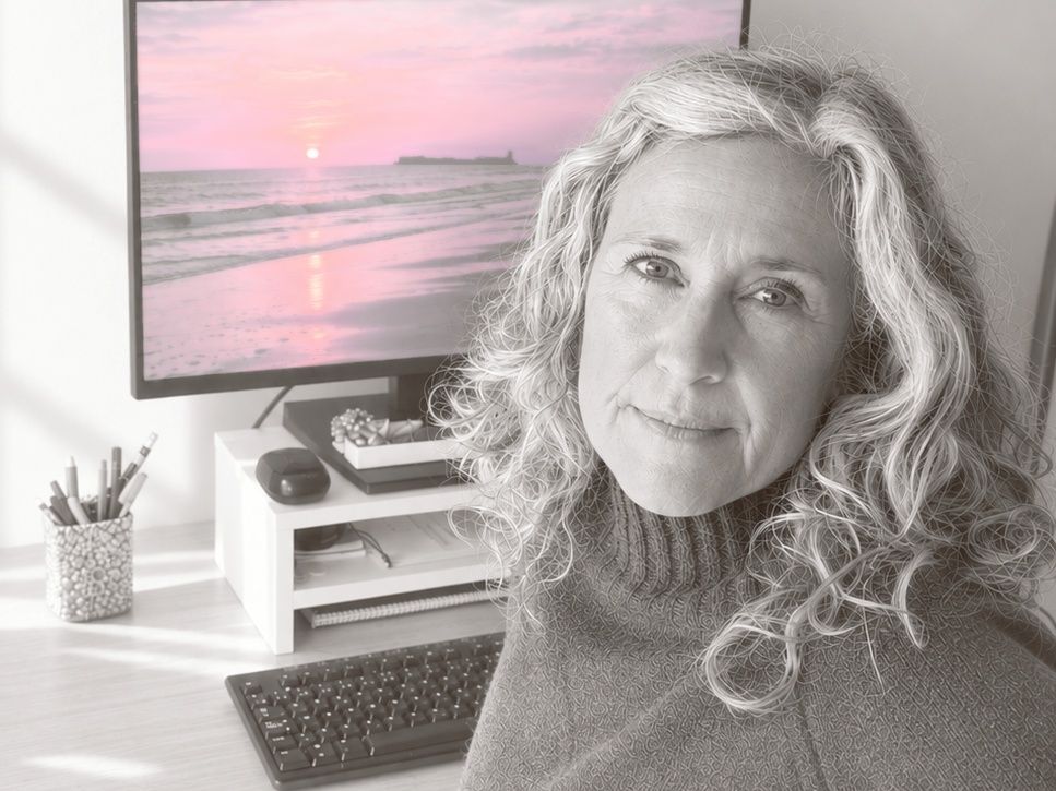Pilar sentada ante su mesa de trabajo, con una puesta de sol rosa en la pantalla del ordenador