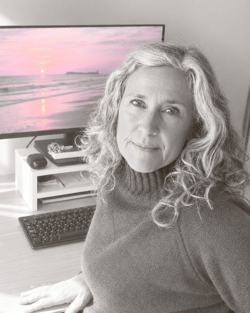 Pilar sentada ante su mesa de trabajo, con una puesta de sol rosa en la pantalla del ordenador